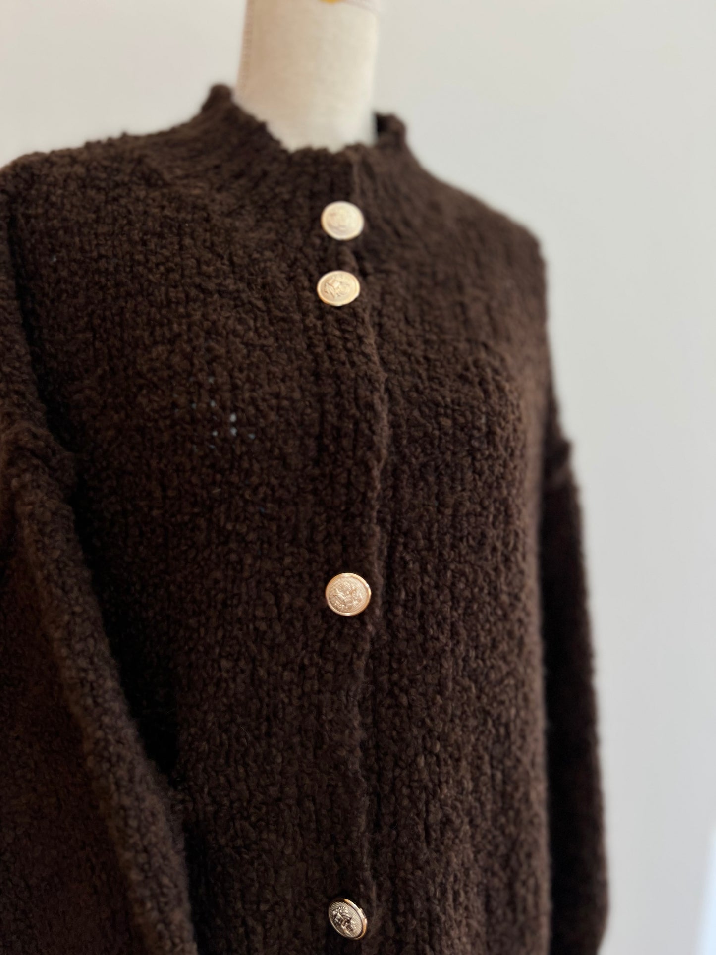 Dunkelbrauner Damen-Cardigan aus festerem Strickmaterial, klassisch geschnitten mit goldenen Knöpfen, eleganter und sportlicher Look.